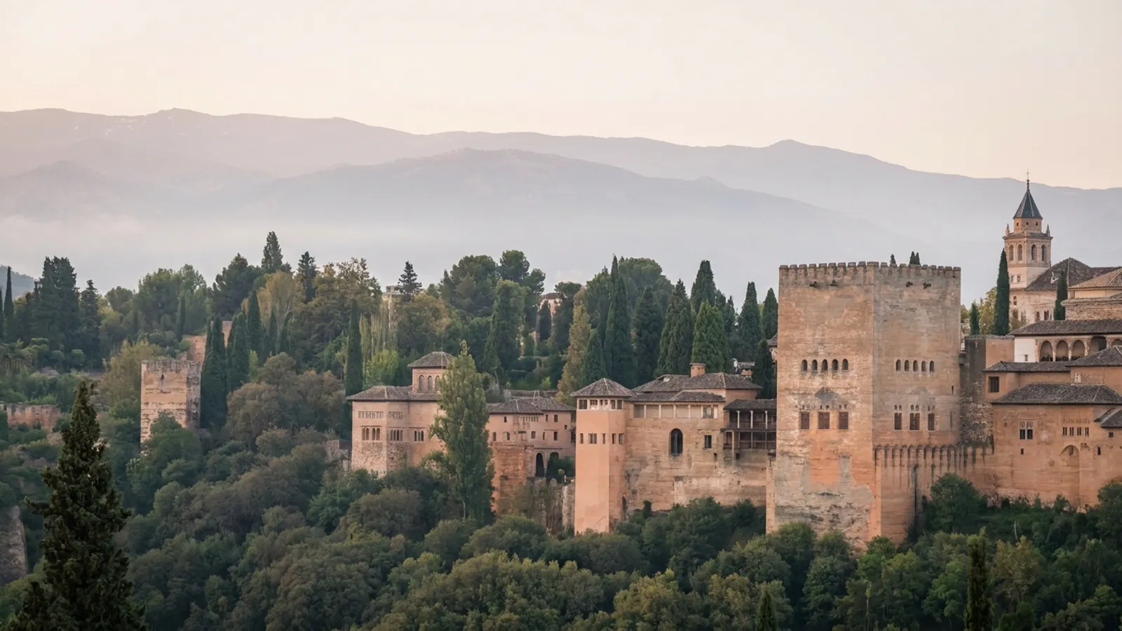 Panoramic view of Granada with the Alhambra under a clear sky, surrounded by verdant hills and snowy peaks in the distance.